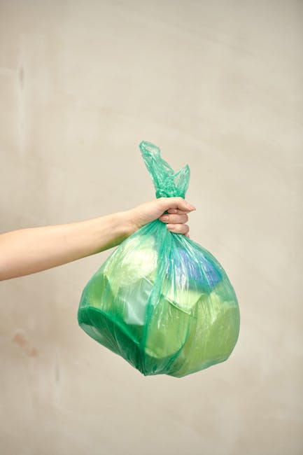 A collection of multiple refuse bags piled against a white plastered exterior wall on a cobblestone pavement. The bags are primarily yellow, white, and transparent, with some containing mixed waste or